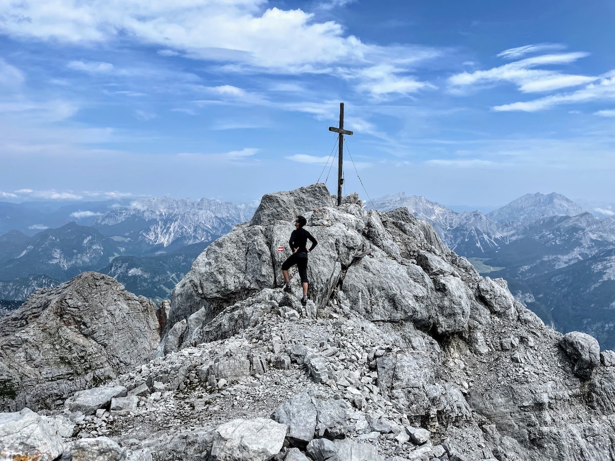 The summit is crowned with a cross. Below us lies a rocky plateau with patches of snow. We could see tiny black figures running across the snow — mountain goats.