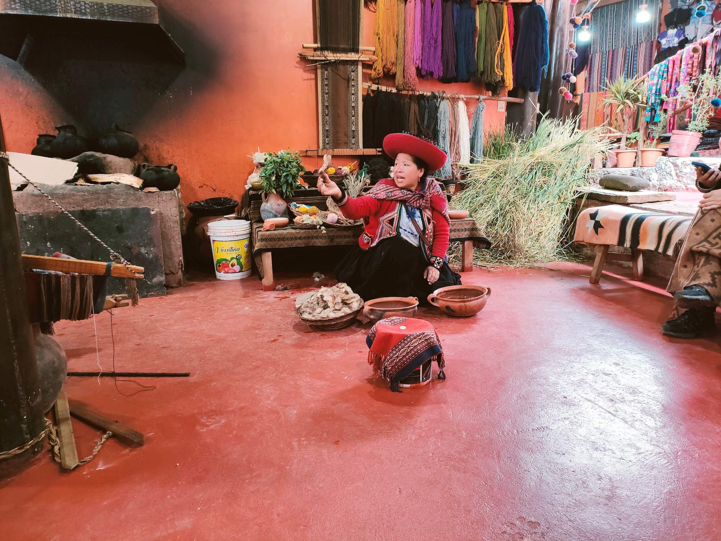A woman demonstrates how wool is washed. Behind her, wool of various colors is hanging.